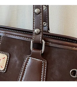 Detailed close-up of brown leather bag with white contrast stitching and silver ring