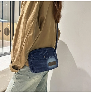 Détail d'un sac bandoulière en denim bleu vintage avec poche à rabat et écusson en cuir