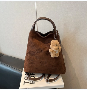 Détail du sac à main en daim marron foncé avec logo Ninaite et breloque ours en peluche