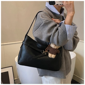 Détail d'un sac à bandoulière noir mat avec garniture dorée et charm d'ours peluche