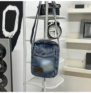 Macro shot of vintage washed denim crossbody bag featuring metal button and leather logo tag