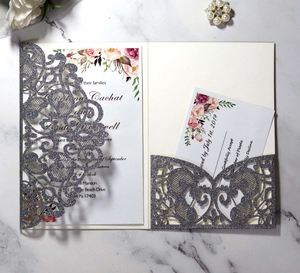 Close-up of laser-cut silver glitter wedding invitation with floral insert on marble background