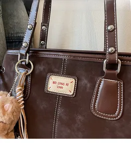 Detail of brown suede tote bag featuring silver rivets, contrast stitching and a plush bear charm