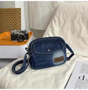 Détail d'un petit sac bandoulière en jean bleu vintage avec écusson en cuir sur tissu blanc