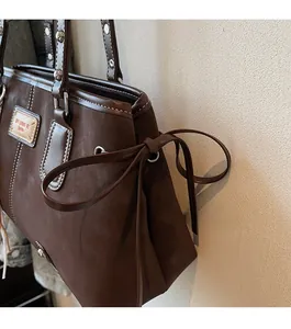 Detail of dark brown suede tote bag featuring side bow knot and white contrast stitching