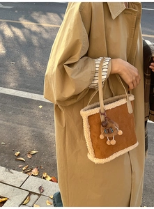Détail d'un sac à main en daim caramel avec bordure en peluche blanche et pendentif ours