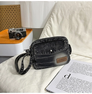 Détail d'un sac bandoulière en denim noir délavé avec écusson en cuir et poches zippées