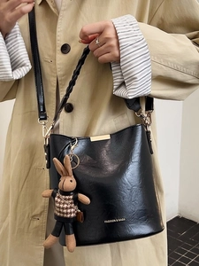 Minimalist black bucket bag with gold accents and a decorative knitted rabbit pendant