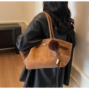 Detail of a brown suede tote bag with a soft fur pom-pom and colorful ethnic bead pendant