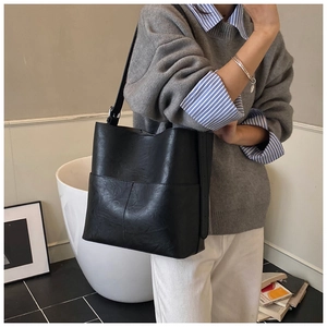 Dettaglio della borsa a secchiello in pelle nera con cuciture a croce e texture liscia