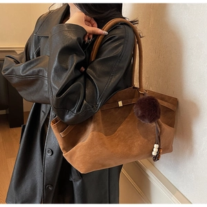 Close-up of caramel suede tote bag with brown pom-pom and wooden bead tassel details