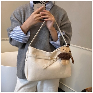 Détail du sac hobo en cuir crème texturé avec boucle dorée et pendentif ours en peluche
