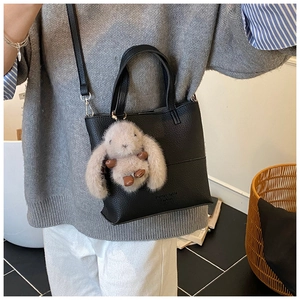 Close-up of black litchi pattern leather tote with cute grey plush rabbit charm detail