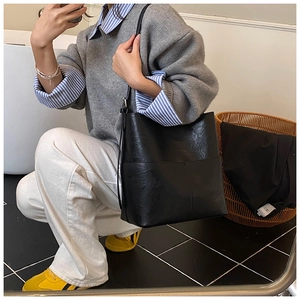 Dettaglio di una borsa a secchiello nera minimalista con tracolle regolabili e finitura opaca in ecopelle