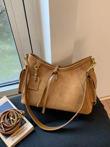 Brown suede crossbody bag with decorative leather strap and golden hardware on a black surface