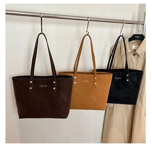 Three retro tote bags in brown and black leather hanging from a stainless steel rack