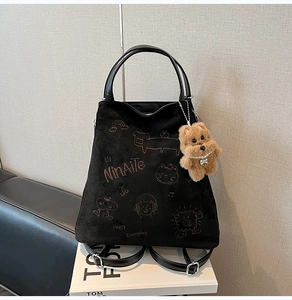 Détail d'un sac à dos en daim noir avec broderie chat et porte-clés chien en peluche