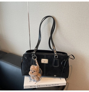 Detail of black suede tote bag with white contrast stitching and cute teddy bear charm