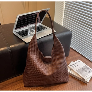 Detailed view of dark brown woven leather tote with wide shoulder strap in office setting