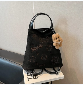Détail d'un sac à dos en daim noir avec broderies cartoon et charm ours en peluche