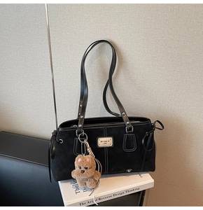 Detail of vintage matte black tote bag with white stitching and brown bear pendant