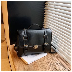 Close-up of vintage black messenger bag with gold buckles and push-lock on a wooden desk