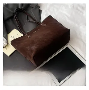 Detail view of large dark brown suede tote bag with metal nameplate on white fabric