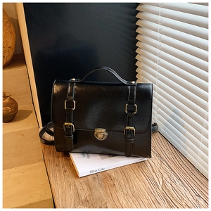 Close-up of retro black satchel bag with bronze buckles on a wooden surface