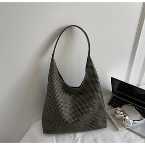 Detail of dark green woven hobo bag next to a laptop and book for a modern office look