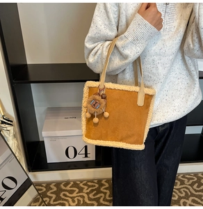 Détail d'un sac cabas en daim marron avec bordure en polaire blanche et breloque lion
