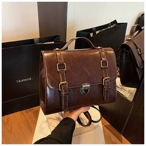 Detail of dark brown leather messenger bag with bronze hardware and buckle straps