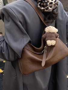 Sac hobo en cuir marron avec breloque ours, porté sur un mannequin en costume gris