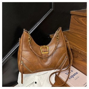 Detail der braunen Kunstledertasche mit Metallketten griff und goldener Schnalle auf Holztreppen
