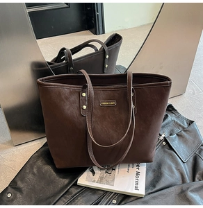 Detail of dark brown leather tote bag featuring a gold metal nameplate and fine texture