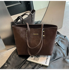 Close-up of chocolate brown tote bag with gold logo plate on a leather jacket background