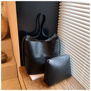 Dettaglio del set borsa a secchiello in pelle opaca nera con tracolla larga e pochette