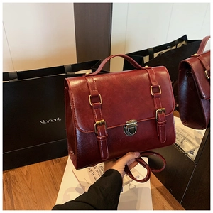 Close-up of vintage burgundy messenger bag with dual straps and metal press buckle