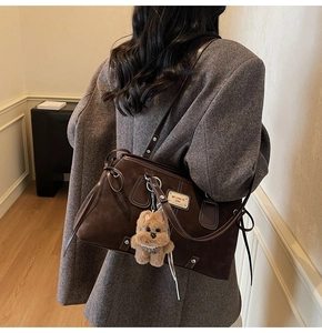 Detail of dark brown suede tote bag with gold vintage plaque and plush dog charm