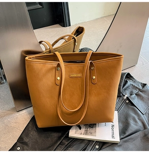 Close-up of caramel brown tote bag with metal nameplate on stylish black leather jacket