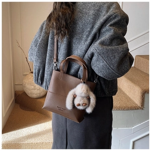 Close-up of a brown litchi pattern bucket bag with a cute white plush bunny charm