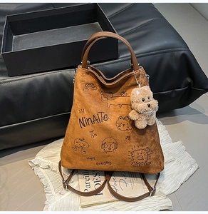 Détail du sac en daim marron avec imprimés de dessins animés et pendentif chien peluche