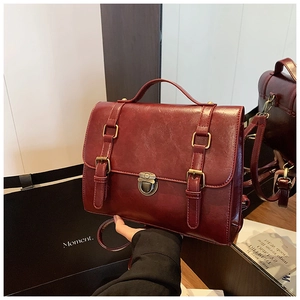 Detail view of deep red vintage messenger bag with gold buckles and metallic lock