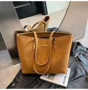 Detailed macro view of the brown leather tote bag showing a gold fashion metal nameplate