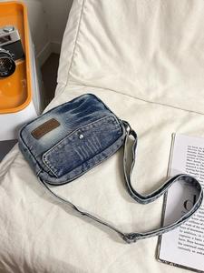 Retro denim blue crossbody bag with metal rivets on a white textured background