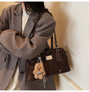 Detail of coffee brown tote bag with white stitching and plush puppy pendant accessory