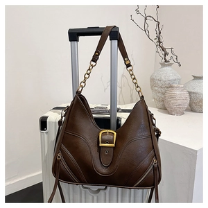 Detail einer braunen Leder-Tote-Bag mit goldener Kette auf einem weißen Reisekoffer