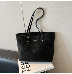 Macro shot of black PU leather tote bag with gold hardware and embossed fashion logo