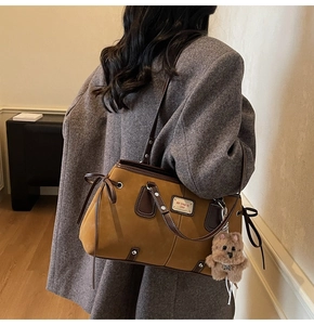 Detail of vintage suede tote bag showing brand metal plate and plush bear charm decoration