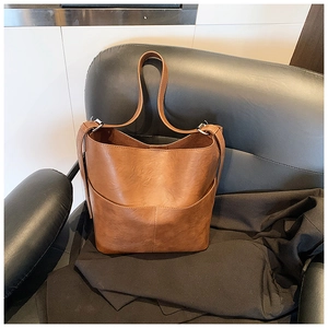 Dettaglio di una borsa a secchiello marrone con grana litchi fine e cuciture pulite sulla pelle