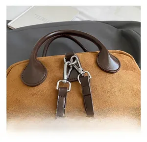 Détail du crochet en métal argenté et de l'anse en cuir marron sur le sac en daim caramel